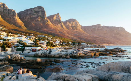 Tranquil coastal view of Bakoven Beach in Cape Town, with granite boulders, tidal pools, and the iconic backdrop of the Twelve Apostles mountains—just a scenic drive from Devonport House in Constantia. A serene, less-crowded spot ideal for sunset watchers and nature lovers.