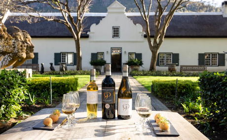 Wine bottles and glasses on a table in a garden courtyard with a historic building in the background