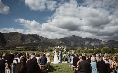 Outdoor wedding ceremony in a vineyard with guests seated and mountains in the background Outdoor wedding ceremony in a vineyard with guests seated and mountains in the background