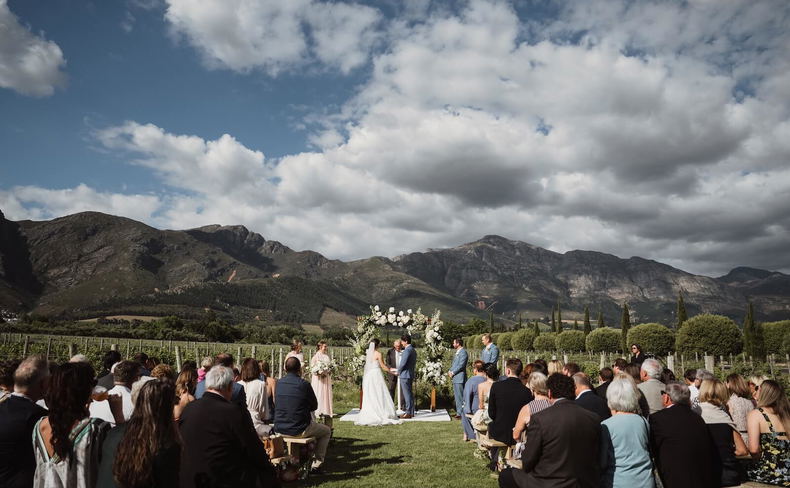 Outdoor wedding ceremony in a vineyard with guests seated and mountains in the background