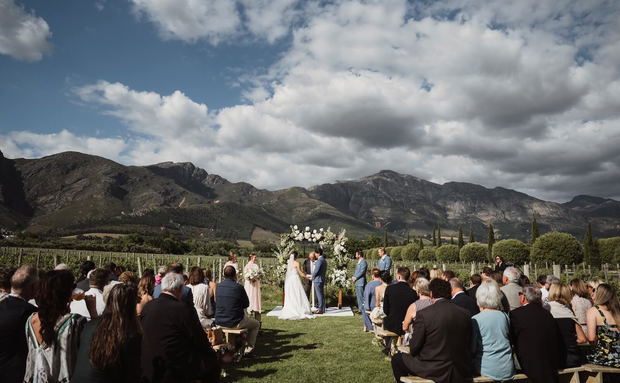 Outdoor wedding ceremony in a vineyard with guests seated and mountains in the background Outdoor wedding ceremony in a vineyard with guests seated and mountains in the background