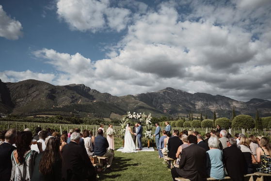 Outdoor wedding ceremony in a vineyard with guests seated and mountains in the background Outdoor wedding ceremony in a vineyard with guests seated and mountains in the background