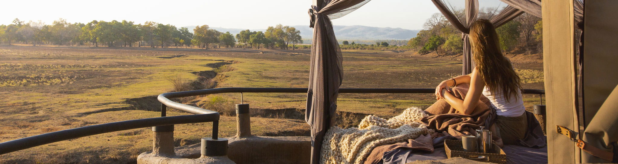 lady on starbed of suite looking out at floodplains of Puku Ridge Camp Zambia