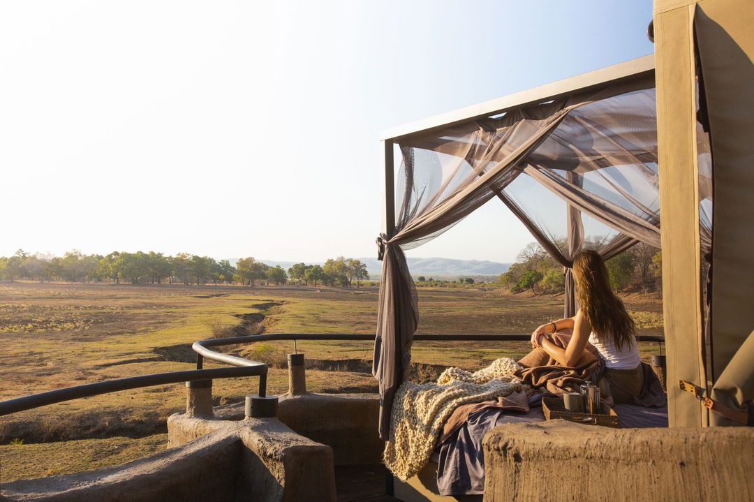 lady on starbed of suite looking out at floodplains of Puku Ridge Camp Zambia