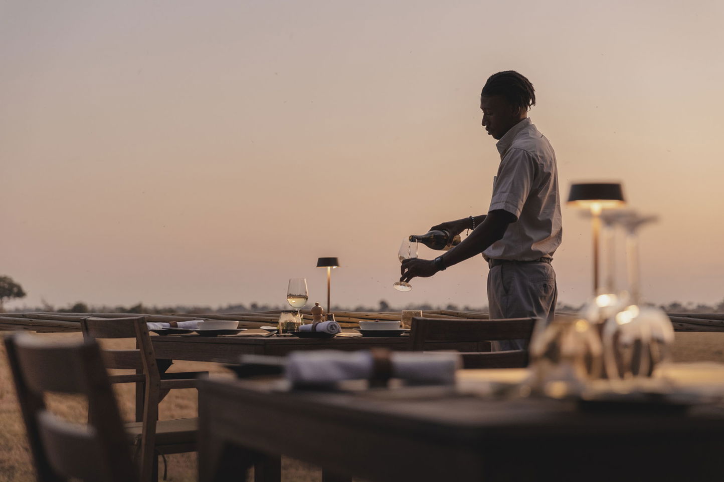 waiter pouring wine on deck at Wilderness Mombo Camp in the Okavango Delta