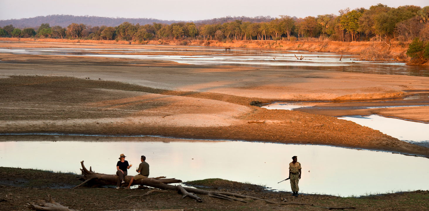 two guest sand guide by river at sunset close to lodge of Puku Ridge Camp Zambia