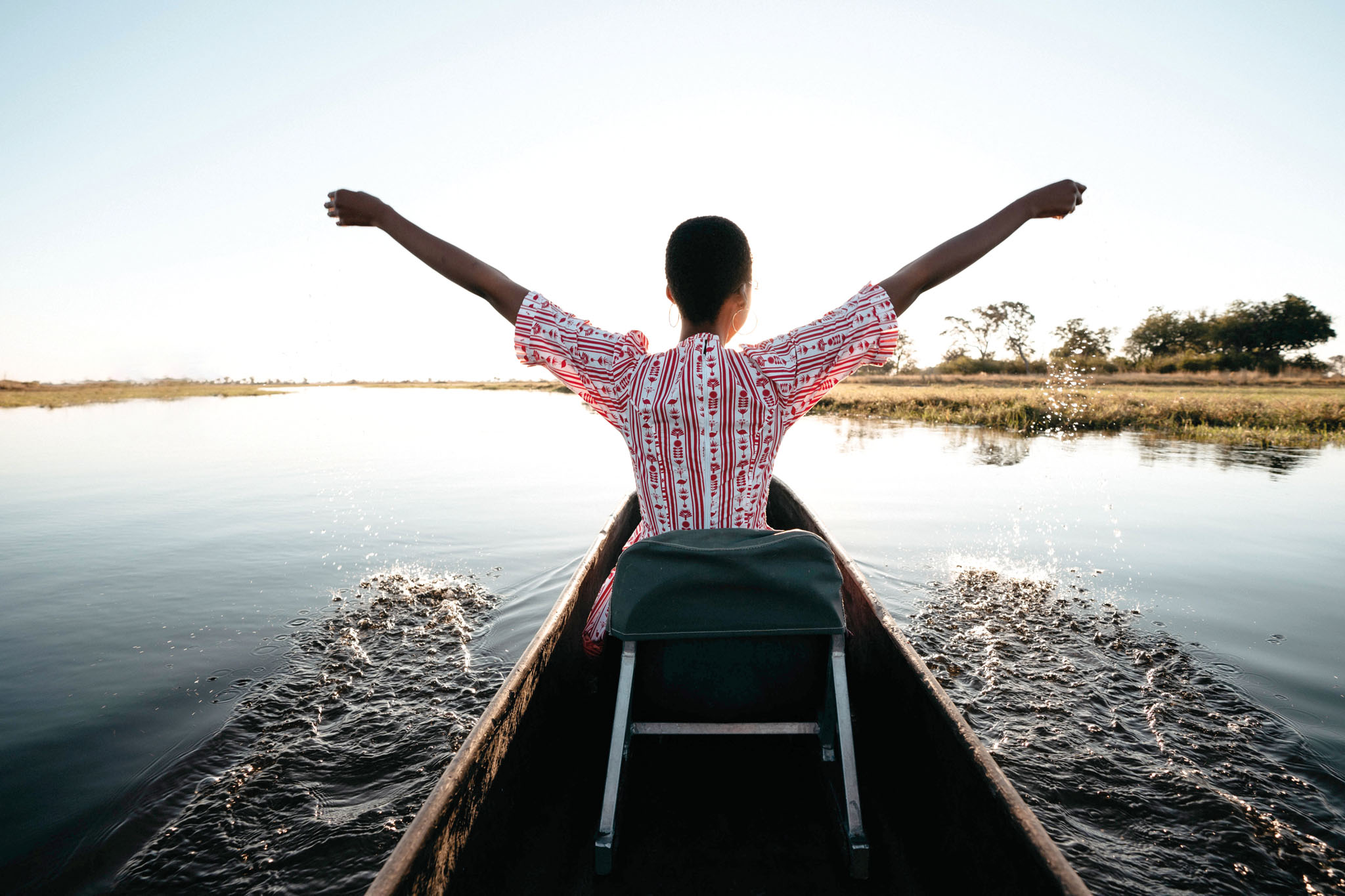 guest with open arms on mokoro on water of delta at Eagle Island Lodge Belmond