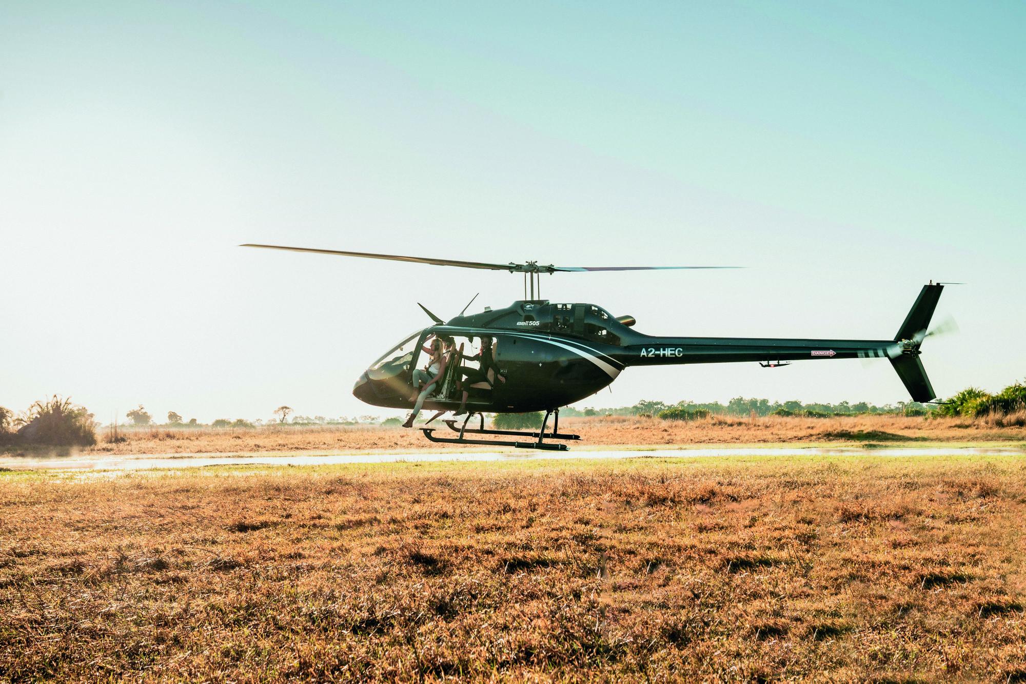 low flying helicopter over Okavango Delta with lady guest partially hanging out at Belmond Eagle Island Lodge