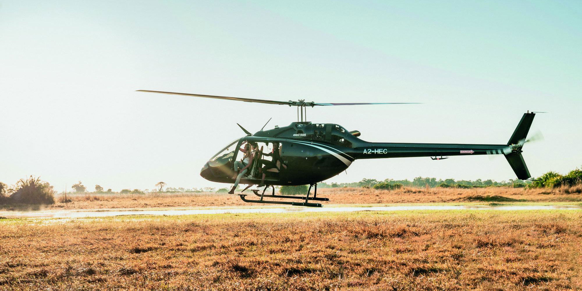 low flying helicopter over Okavango Delta with lady guest partially hanging out at Belmond Eagle Island Lodge