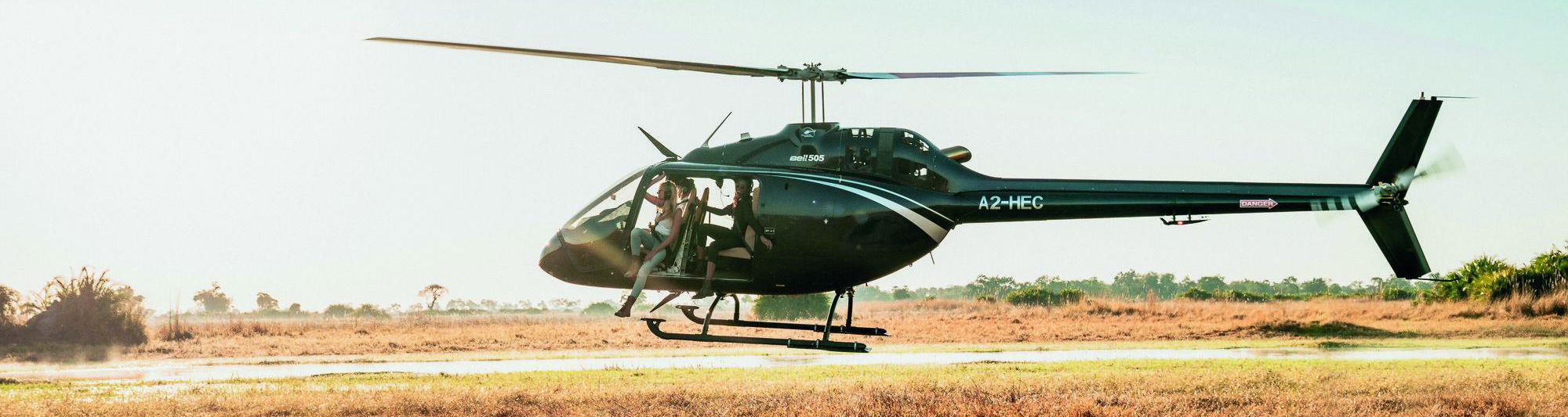 low flying helicopter over Okavango Delta with lady guest partially hanging out at Belmond Eagle Island Lodge