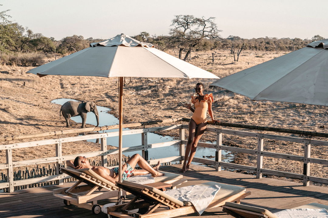 lady guest on pool deck under umbrella with waterhole behind at Savute elephant lodge Botswana