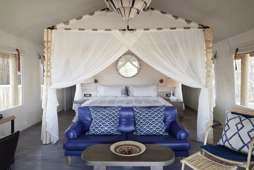 interior of luxury room with double bed and blue couch at Belmond Savute elephant lodge Botswana