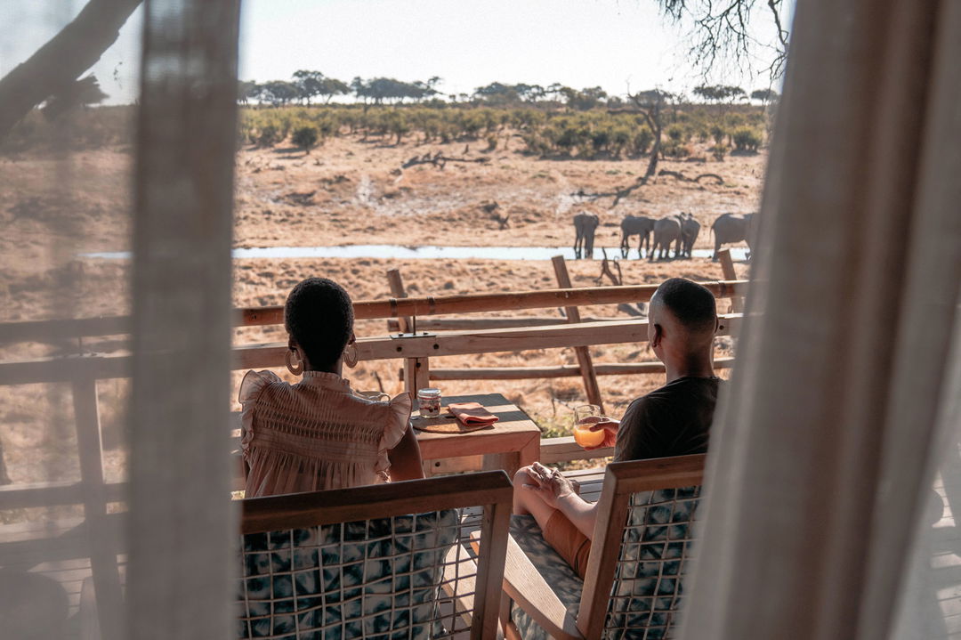 couple guest having breakfast on deck and looking at elephants nearby at Savute elephant lodge Belmond