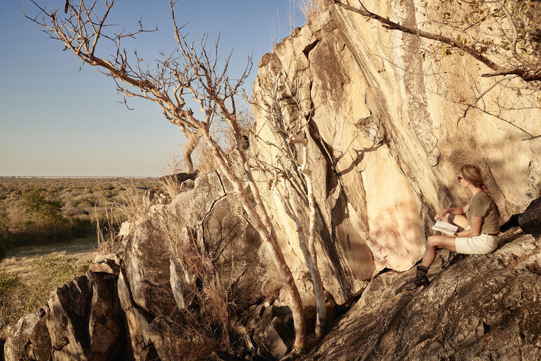 lady guest looking at bushman painting on rock by Savute elephant lodge Belmond