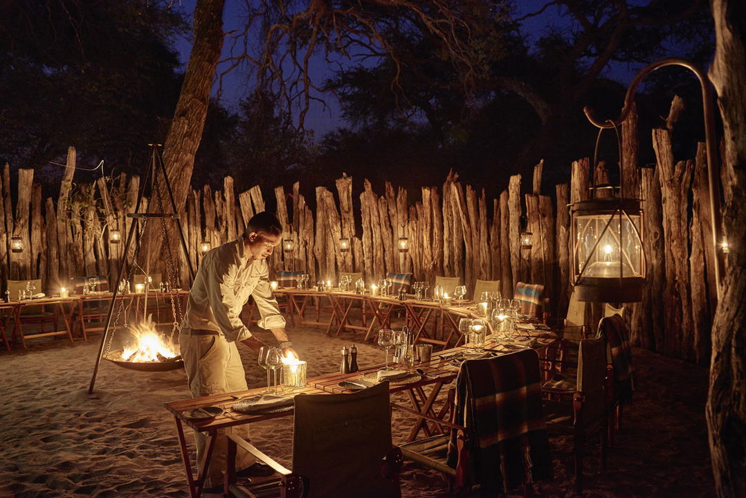 waiter setting tables in African bush boma with fireplace at Savute elephant lodge Botswana