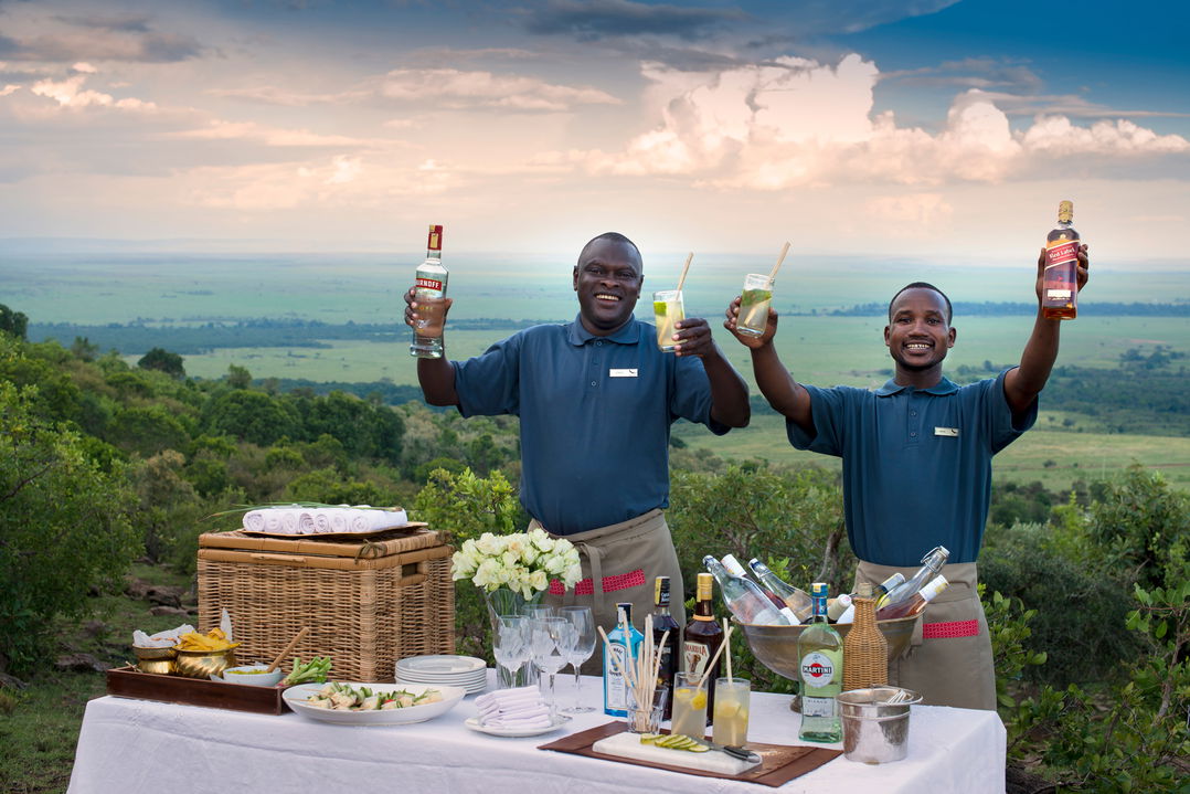 two barmen at a table with drinks for guests at drinks on a tray in bar of andbeyond Bateleur camp Kenya Masai Mara