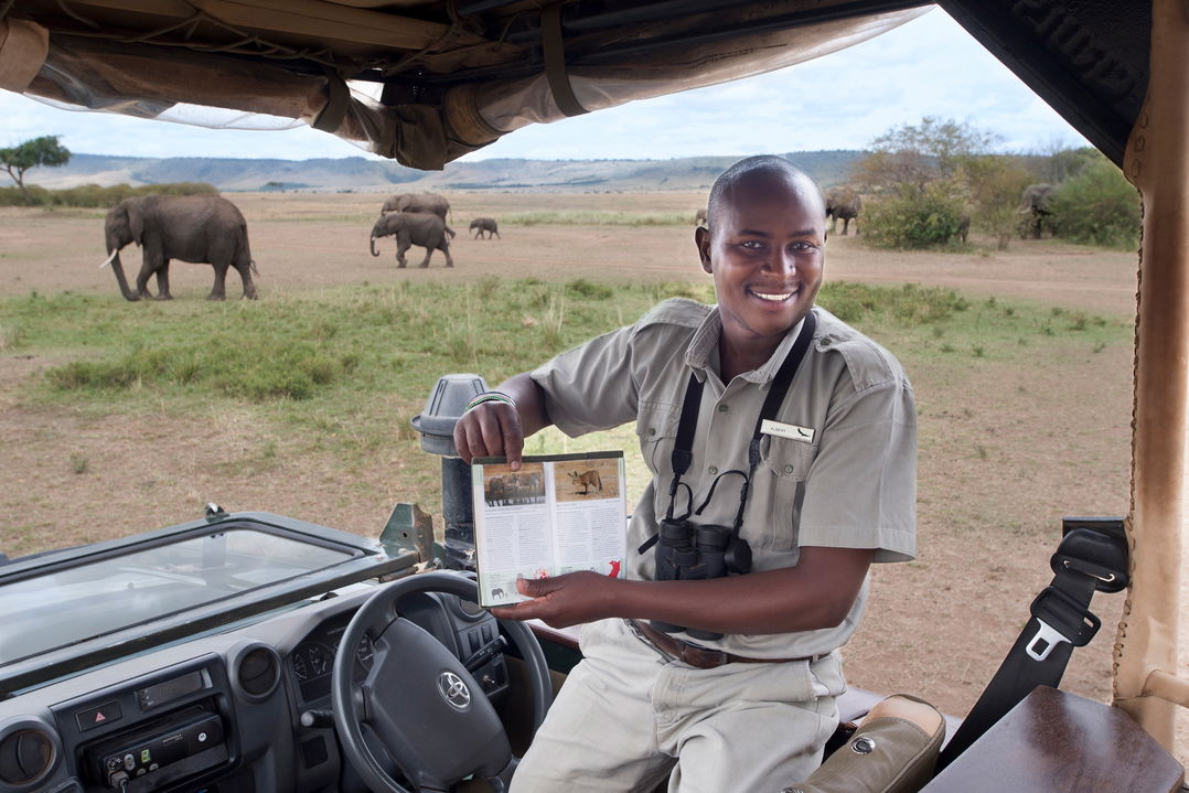 guide with book on safari vehicle education guests at andbeyond Bateleur camp Kenya Masai Mara