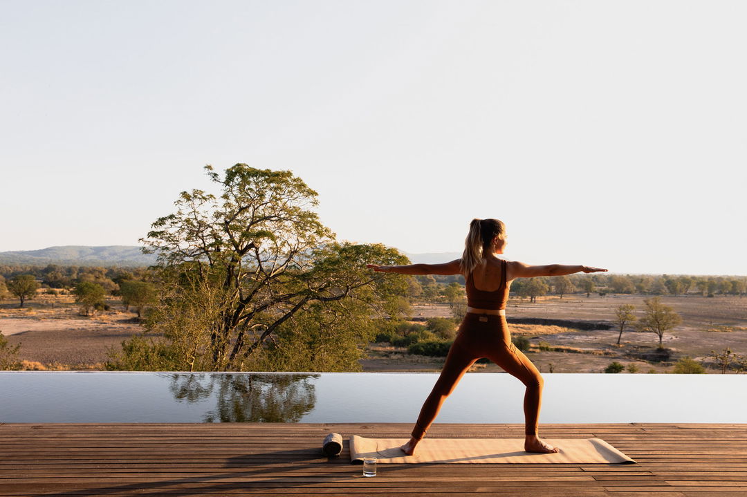 lady guest doing yoga on deck at sunrise by Chichele Presidential Camp Zambia