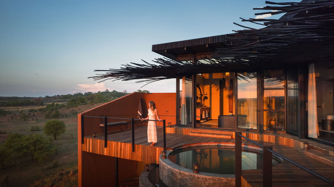 lady on deck of vista suite looking out over plains at sunset by Chichele Presidential Lodge Zambia