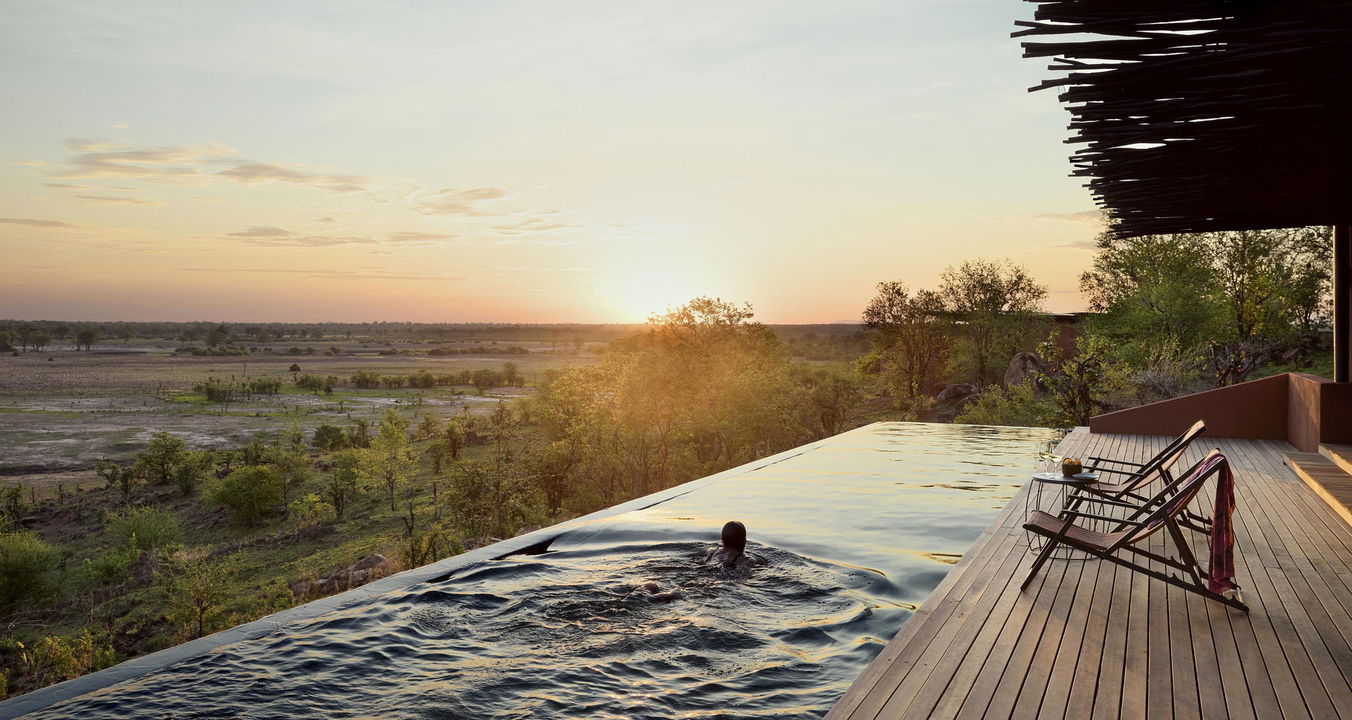 lady guest in pool overlooking plains at sunset by Chichele Presidential Camp Zambia