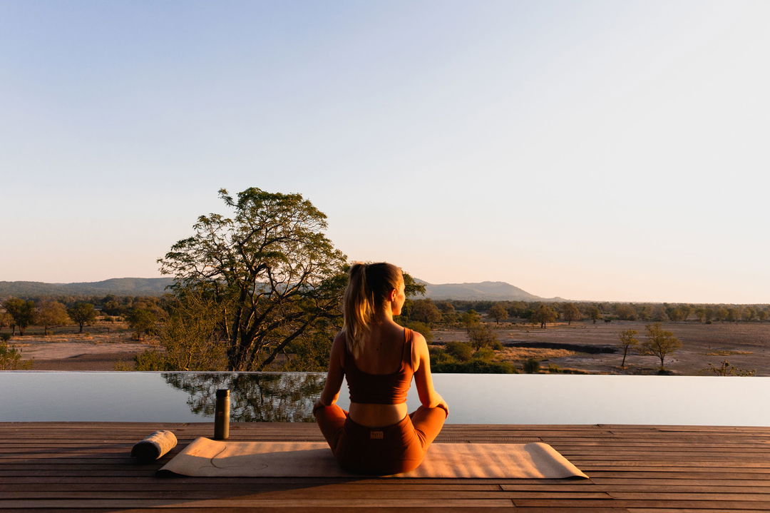 lady guest doing yoga on deck at sunrise by Chichele Presidential Camp Zambia
