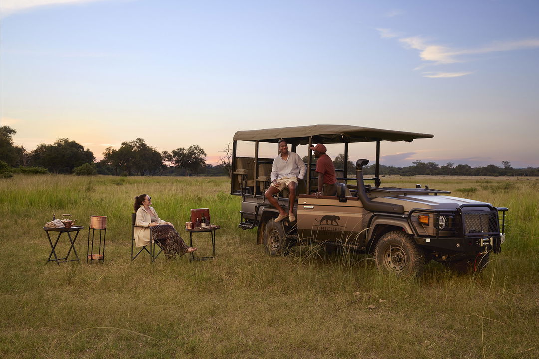 sundowners at sunset by the safari vehicle on plains at Chichele Presidential Camp Zambia
