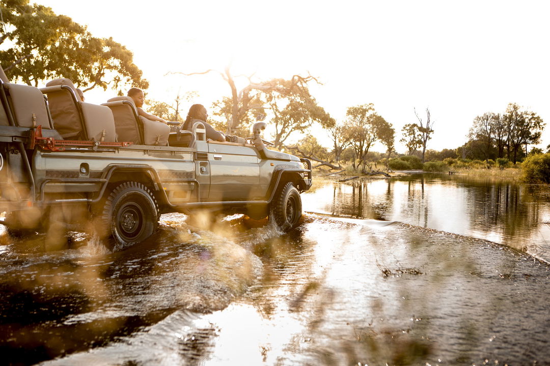 safari vehicle driving through delta water at Vumbura Plains Camp Wilderness Okavango Delta