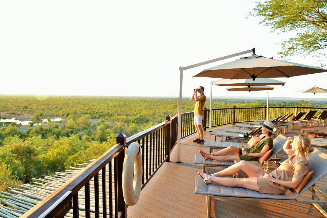 guest with binoculars on deck looking at waterhole by Victoria falls safari lodge