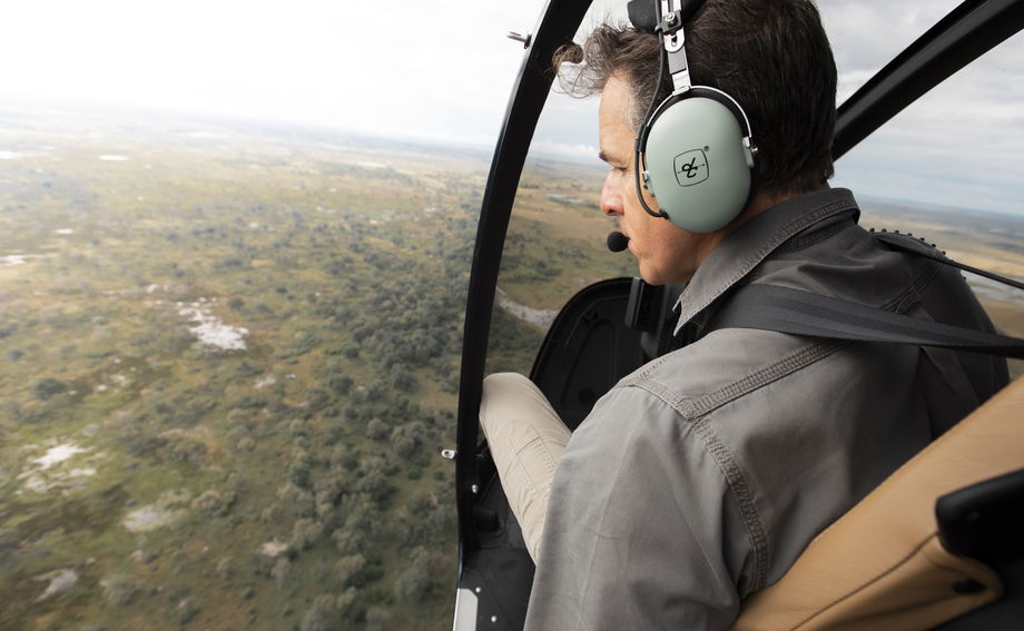 helicopter pilot looking out from flying helicopter at delta below by Vumbura Plains Camp Wilderness Okavango Delta helicopter pilot looking out from flying helicopter at delta below by Vumbura Plains Camp Wilderness Okavango Delta