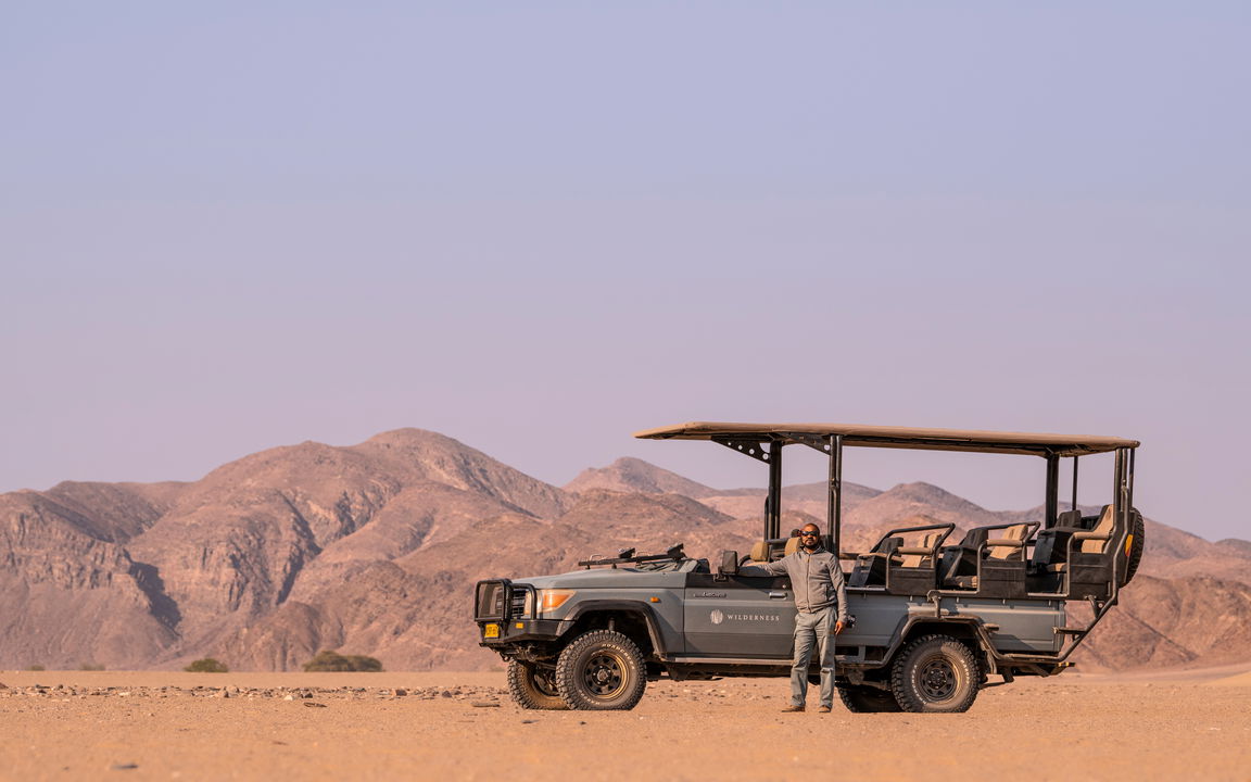 guide standing by safari vehicle with desert mountains in backdrop at Hoanib camp Namibia