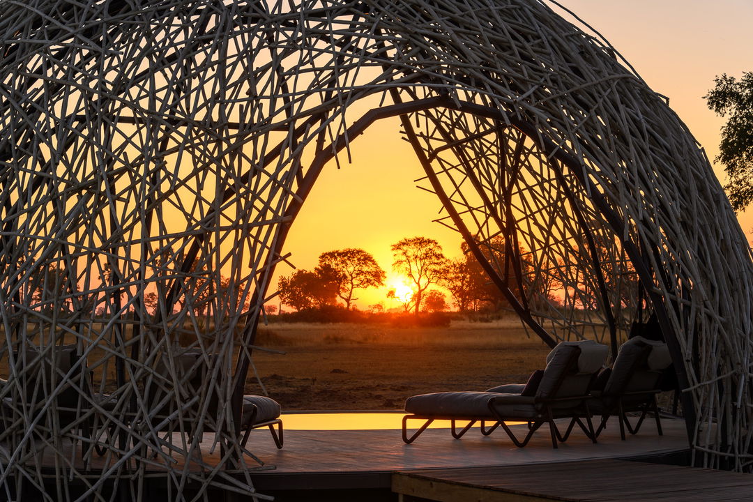 grass dome over pool with sun setting n Okavango delta beyond at Jao Camp Botswana
