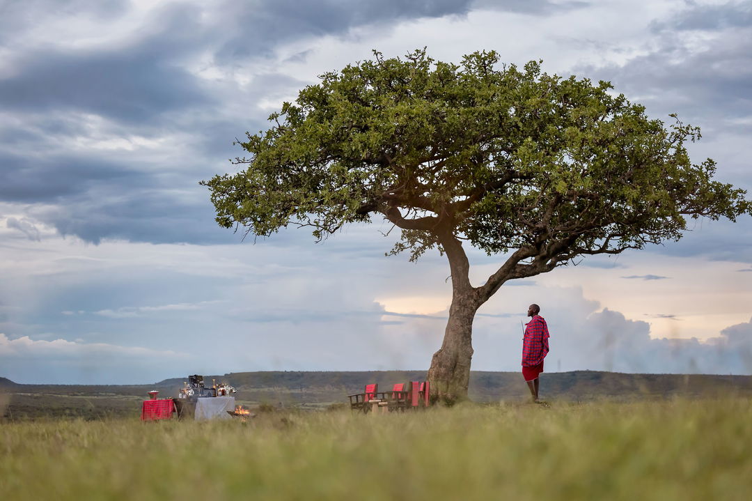 masai man under a tree near a table set for sundowners for guests of the JW Marriot Masai Mara Kenya