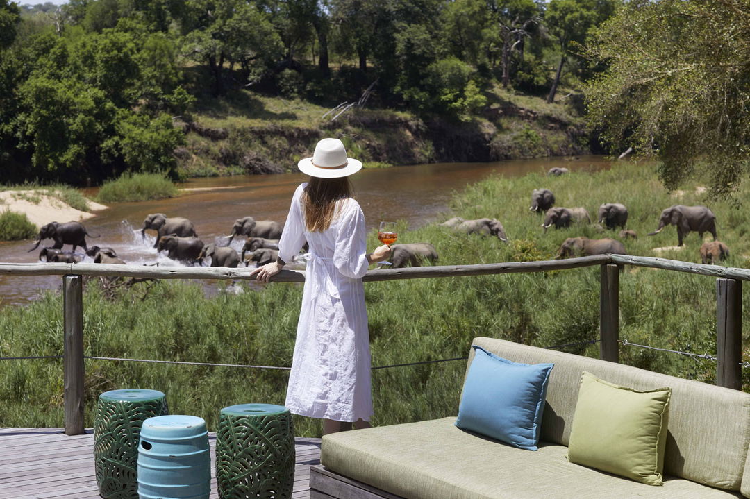 lady guest looking at elephants in river below from deck by Nerina lodge Lion Sands Game Reserve