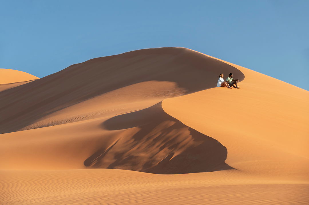 couple sitting on a big sand dune at little Kulala camp wilderness Namibia