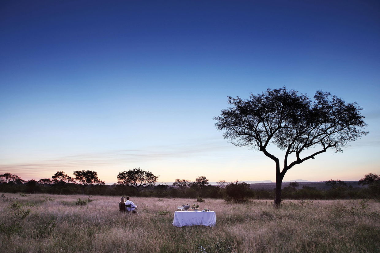couple having sundowners in the bush at sunset by Londolozi game Reserve