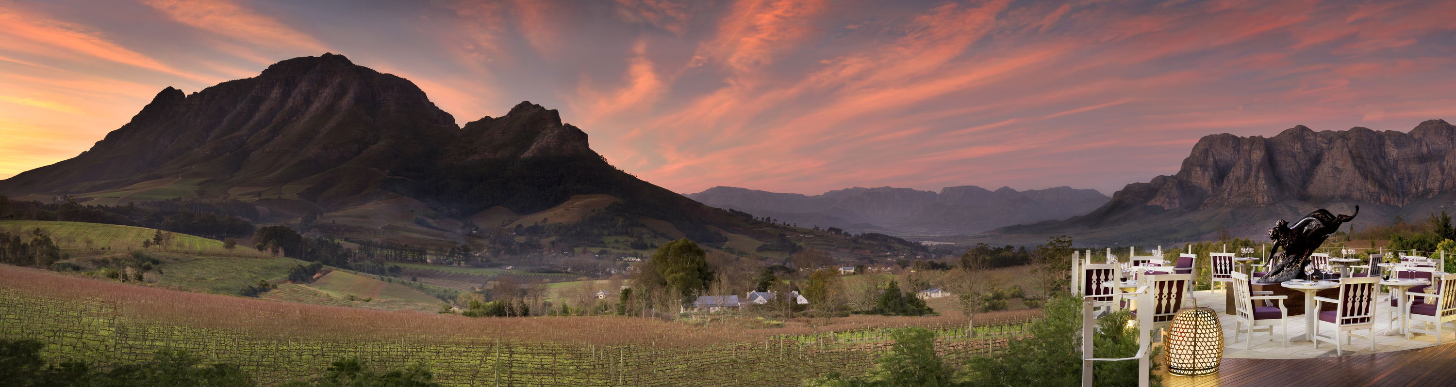 sunset view of Delaire Graff wine estate with tables set for supper and mountains in background