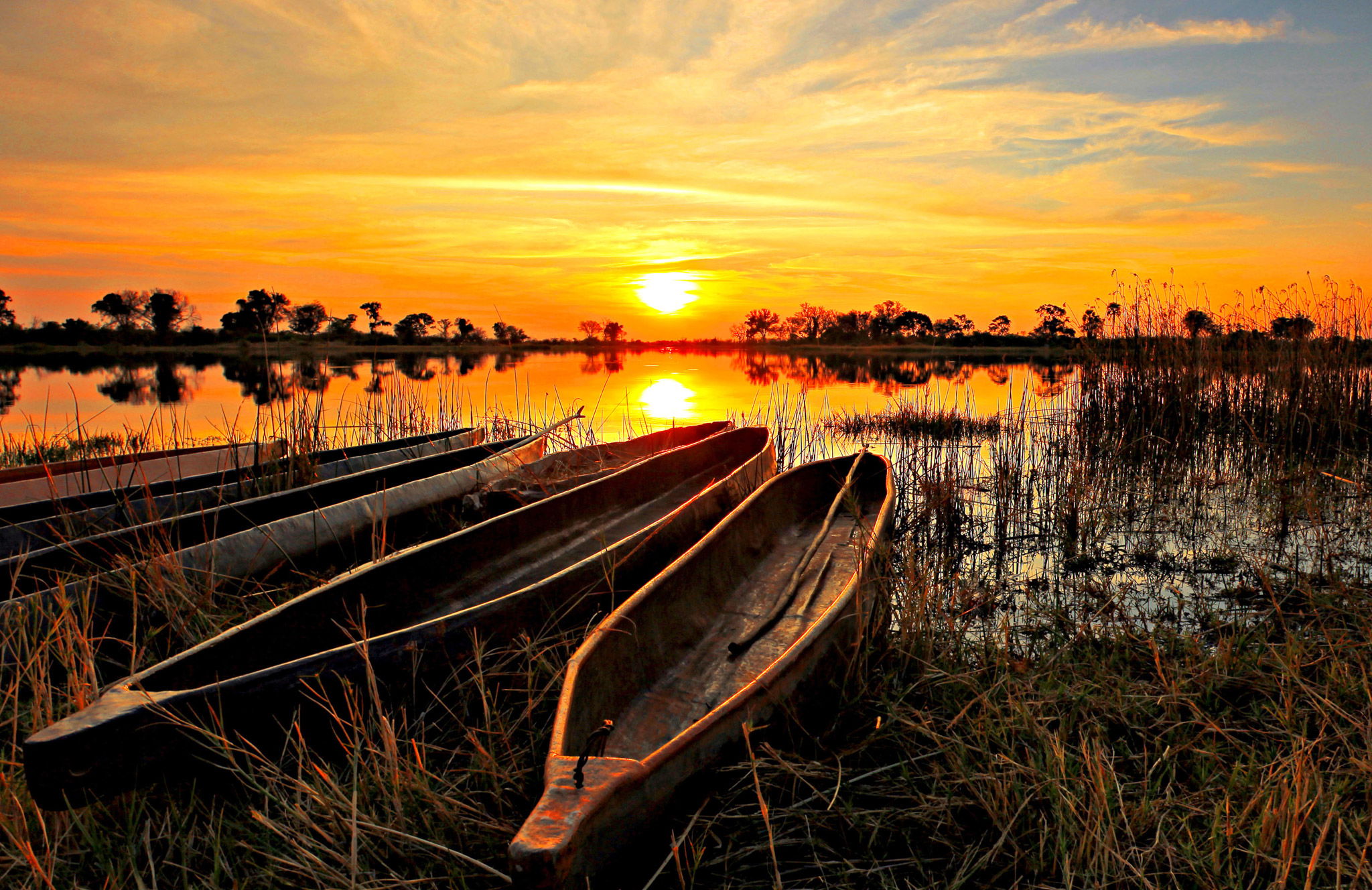 sun setting over Okavango delta with mokoros on riverbank in foreground