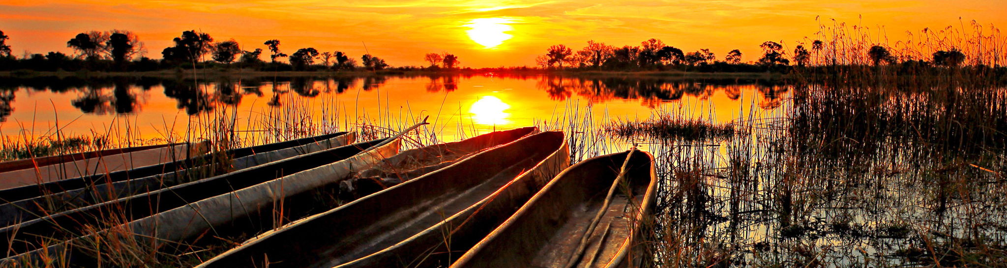 sun setting over Okavango delta with mokoros on riverbank in foreground