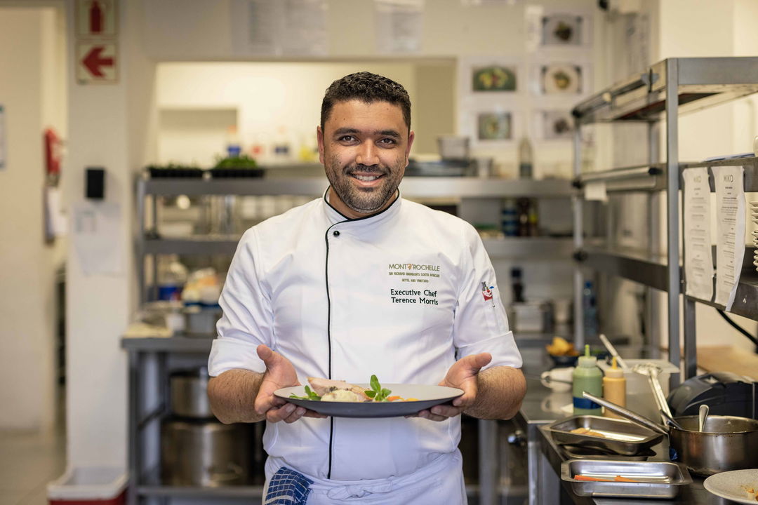 decorated chef with gourmet plate of food standing in kitchen at Virgin Unlimited Mont Rochelle Luxury Hotel in Franshoek