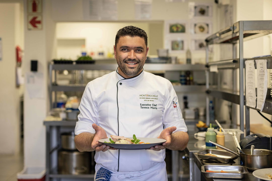 decorated chef with gourmet plate of food standing in kitchen at Virgin Unlimited Mont Rochelle Luxury Hotel in Franshoek