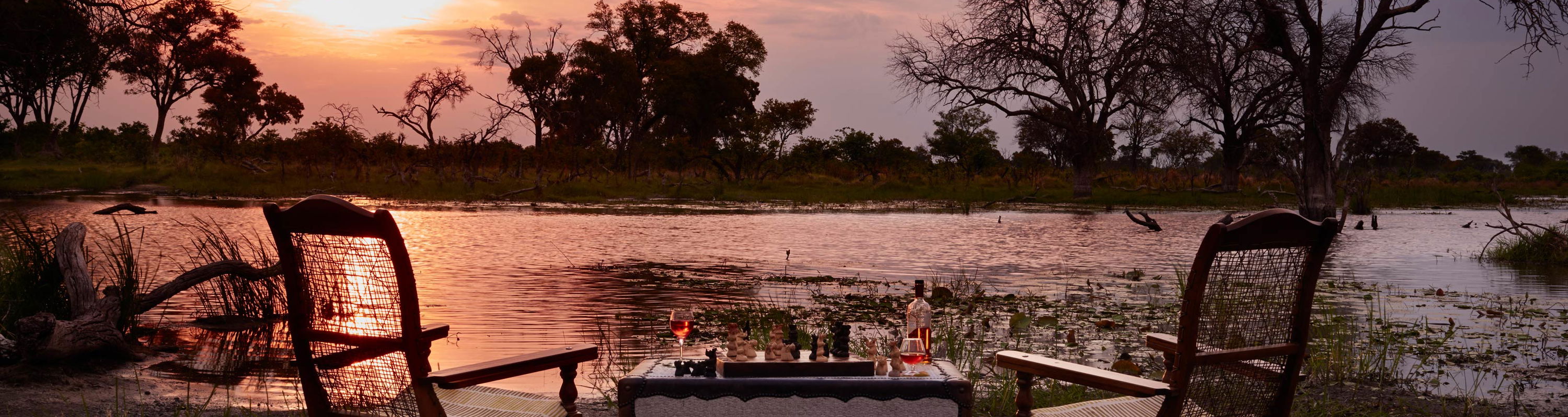 sunset view of table and chairs set with drinks on banks of kwai river lodge Okavango delta