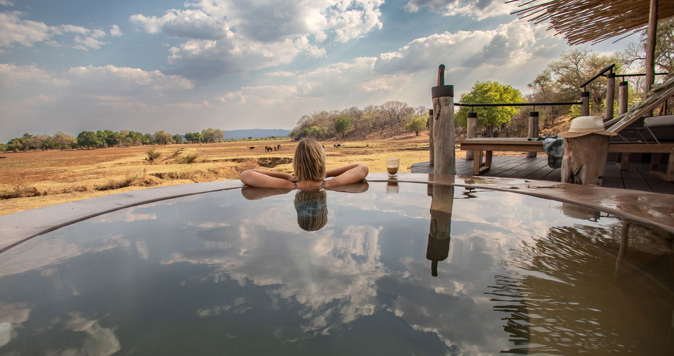lady guest in pool of suite overlooking plains by Puku Ridge Camp Zambia