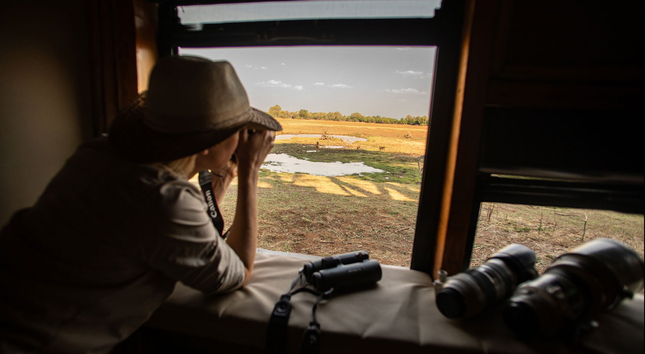 lady in hide looking at wildlife at watering hole by Puku Ridge Camp Zambia Luangwa Plains