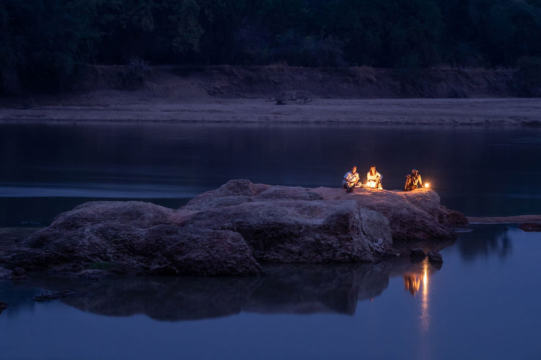 guests sitting by lantern light at night on outcrop of river by Puku Ridge Camp Zambia