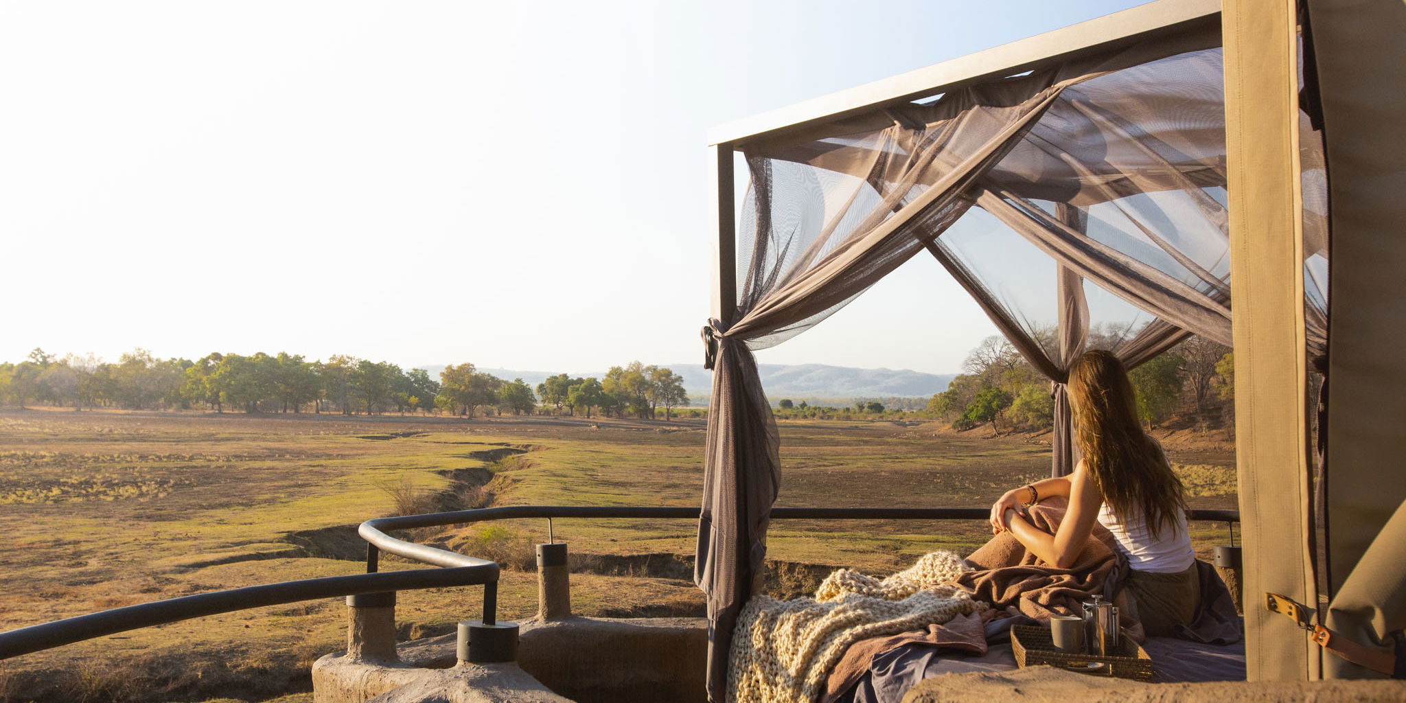 lady on starbed of suite looking out at floodplains of Puku Ridge Camp Zambia