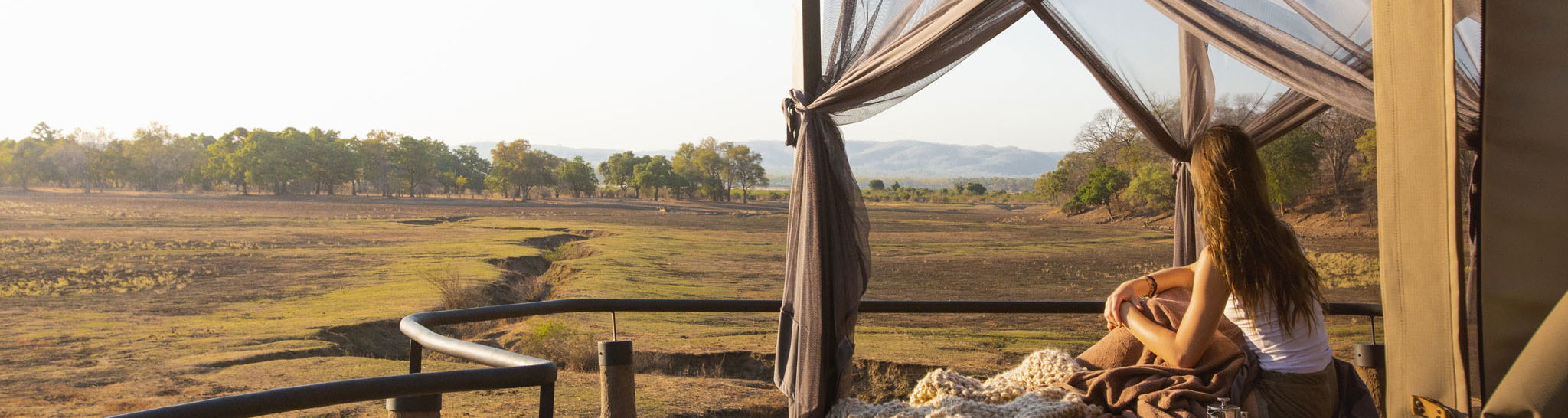lady on starbed of suite looking out at floodplains of Puku Ridge Camp Zambia