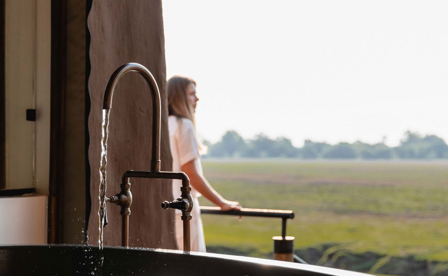 lady running a bath and looking out over plains in Zambia