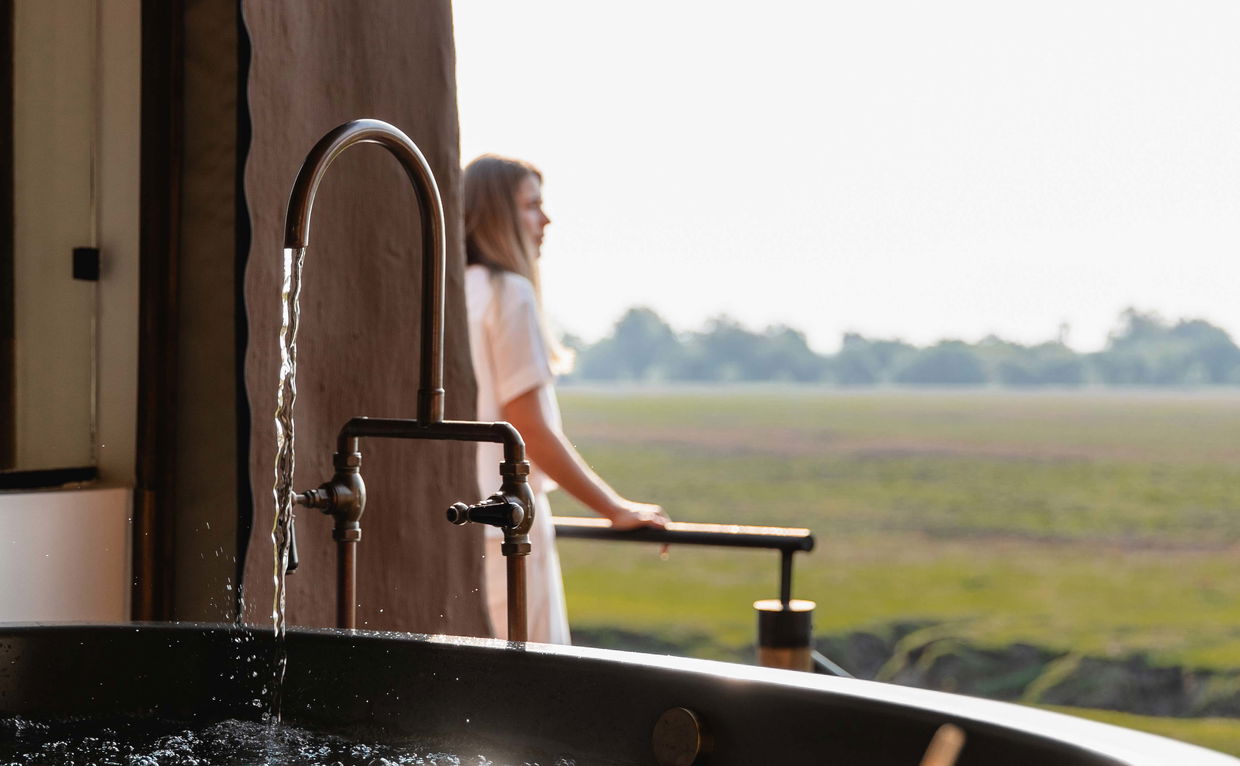 lady running a bath and looking out over plains in Zambia