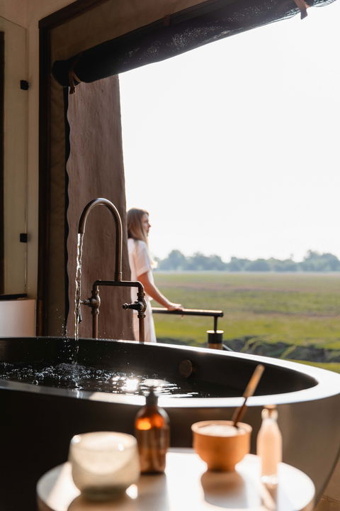 lady running a bath and looking out over plains in Zambia