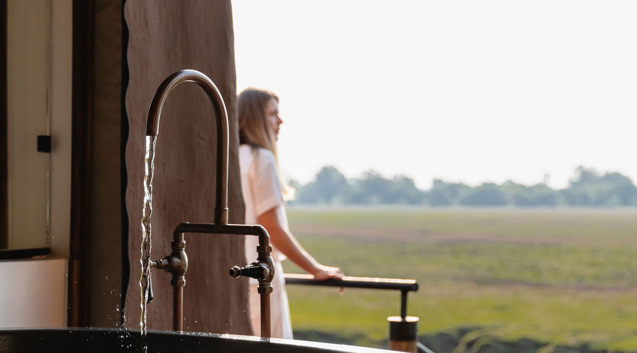 lady guest on deck with bath running in foreground at Puku Ridge Camp Zambia Luangwa Plains